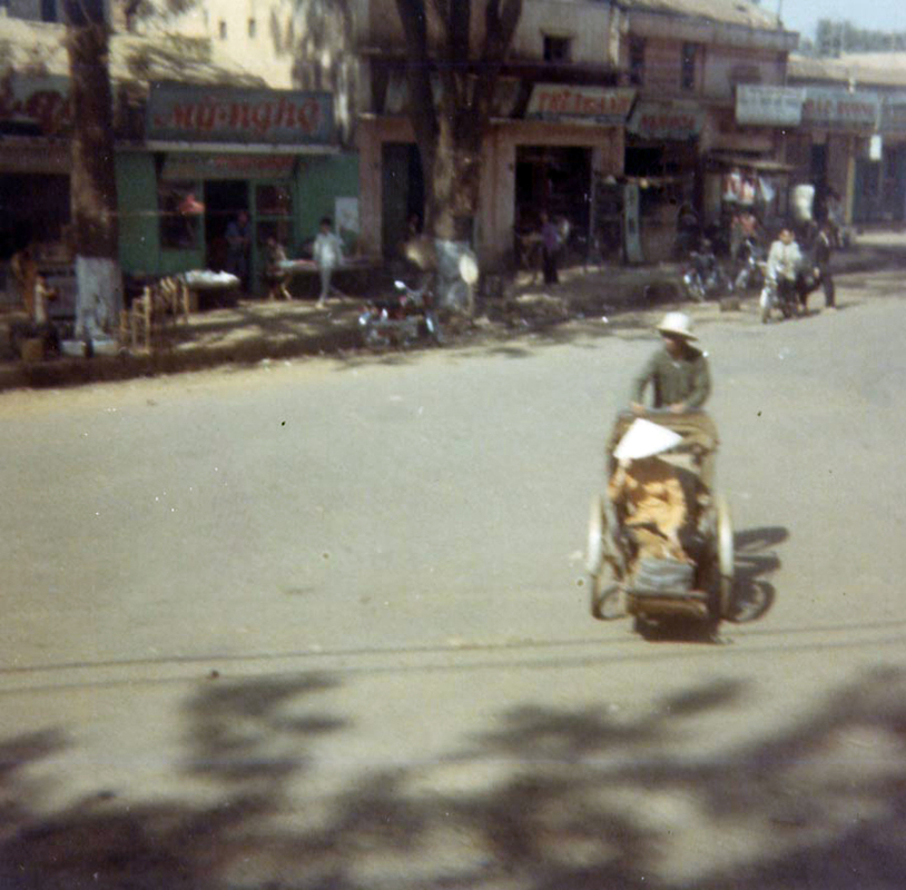 an old po shows people walking on the sidewalk as a motorcycle rides past them