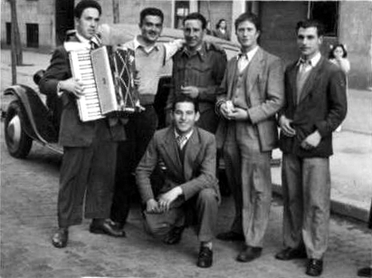 four men are standing outside with an accordion in the street