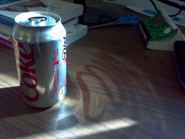 a can of soda sits on a table in front of books and a pen
