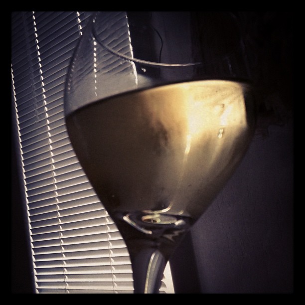 a glass of wine sits beside the blinds on a window