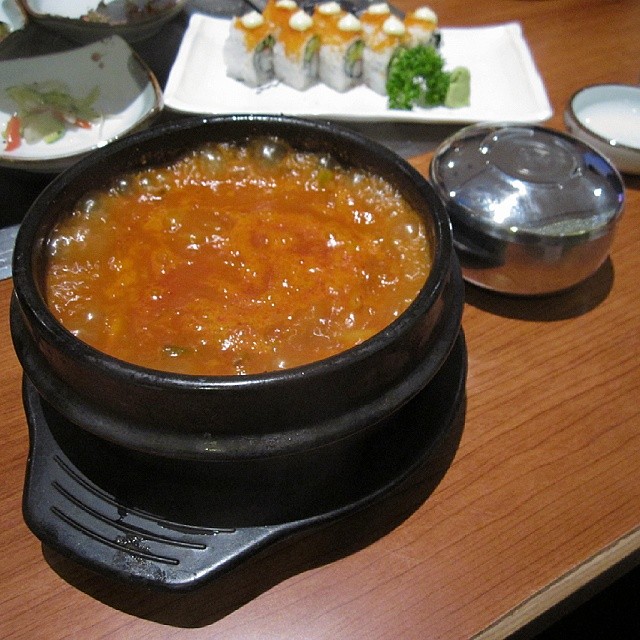 a black dish with soup and vegetables on a table
