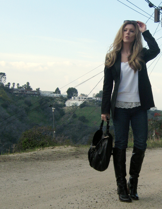 a woman walking across a dirt road holding a hand bag