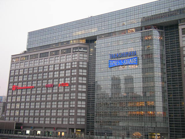 a large glass building with many windows and buildings in the background