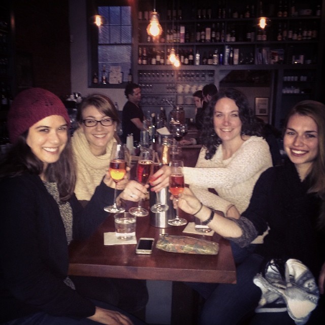three women are sitting at a bar smiling and toasting