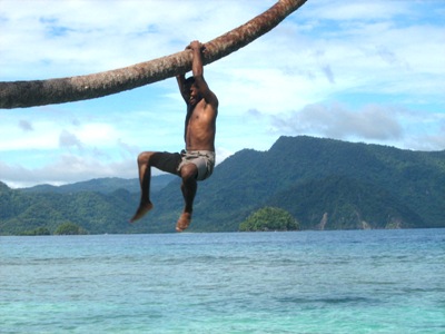 man hanging on the end of a long tree while floating on water