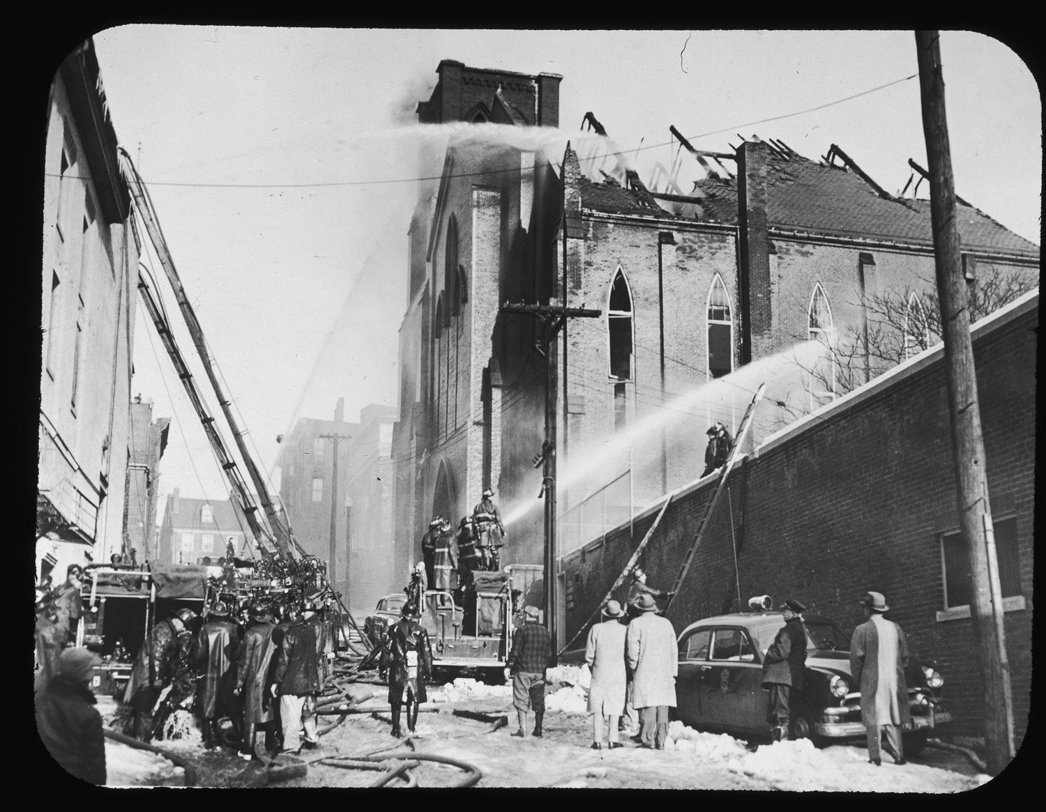 people standing around fire trucks that are pouring water