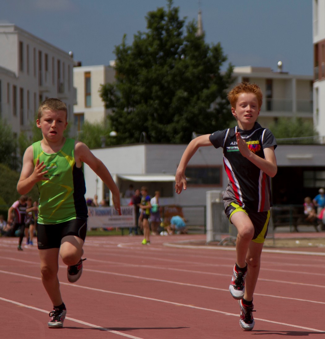 two boys running down a track with others in the background