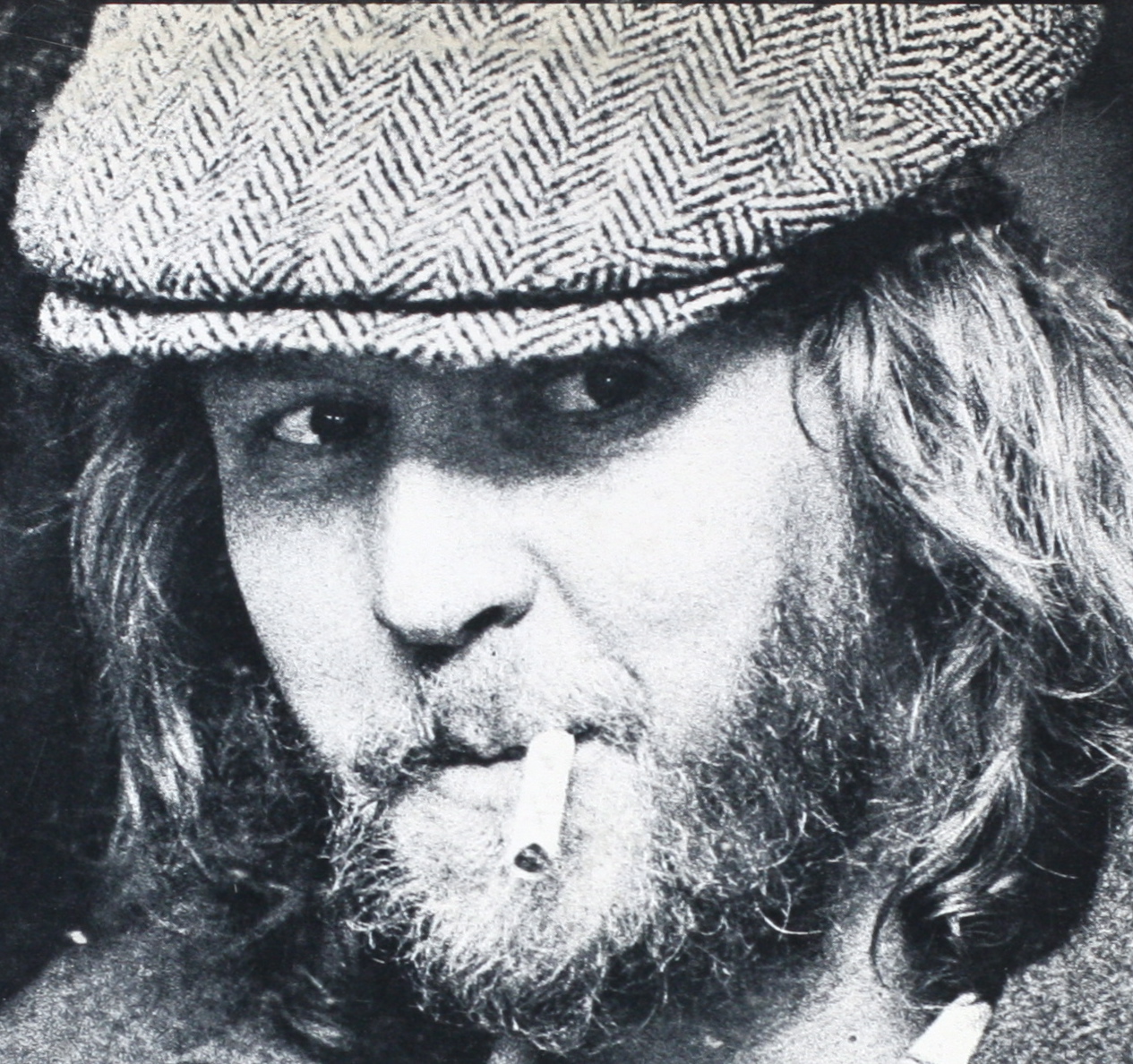a black and white po of a man with long hair wearing a hat and smoking