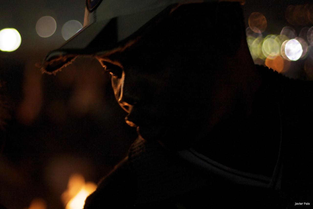 a man wearing a hat in the dark with street lights behind him