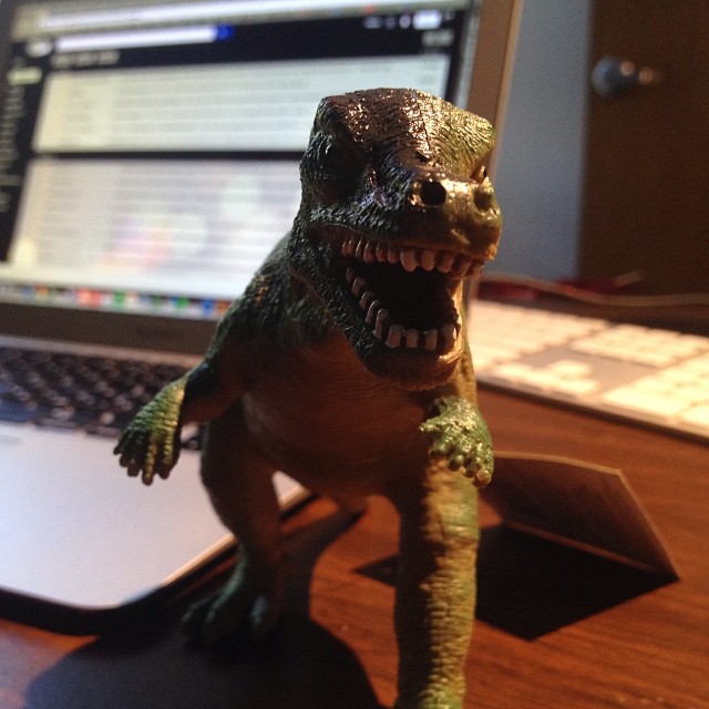 a toy dinosaur sitting on top of a laptop