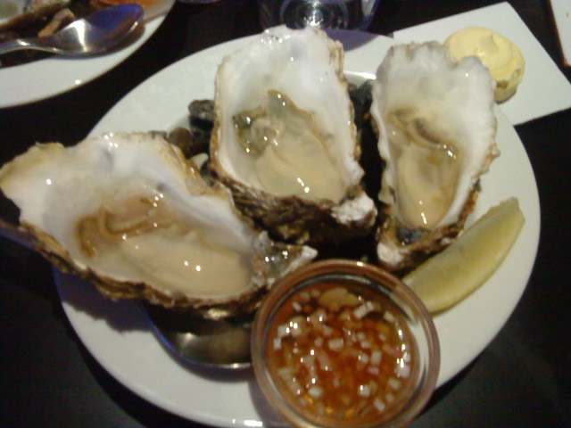 three large oysters with some dipping sauce on the side