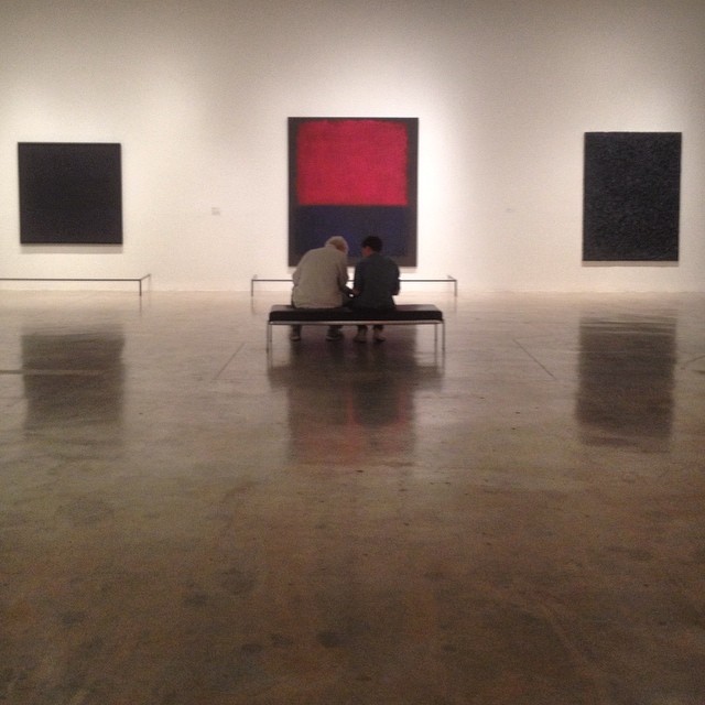 two people are sitting on a bench near two large paintings