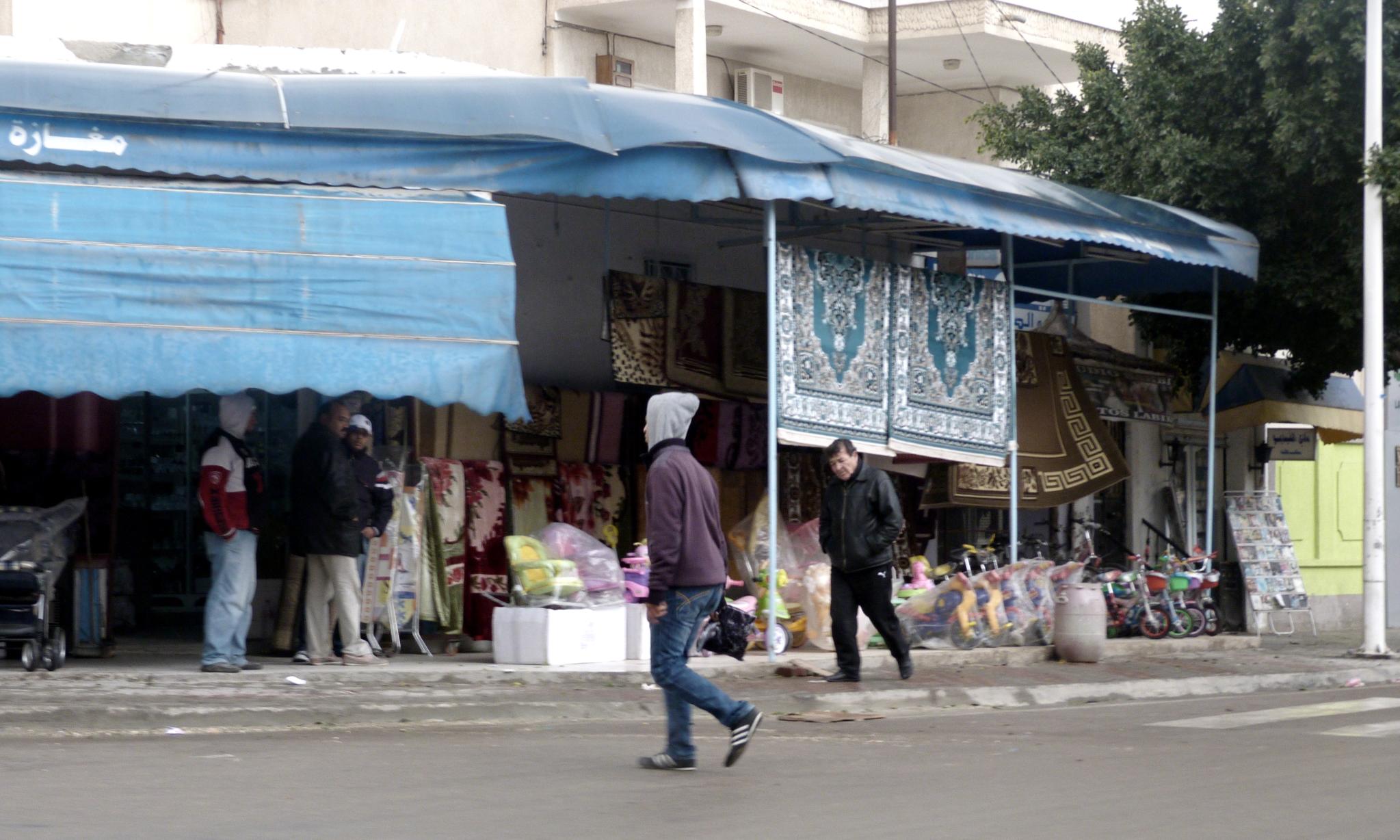 a street vendor walking past a shop where there are people on the side walk