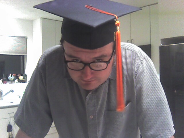 a man looks down as he wears a graduation cap and a tassel