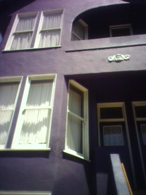 two windows with white shutters are next to a purple building