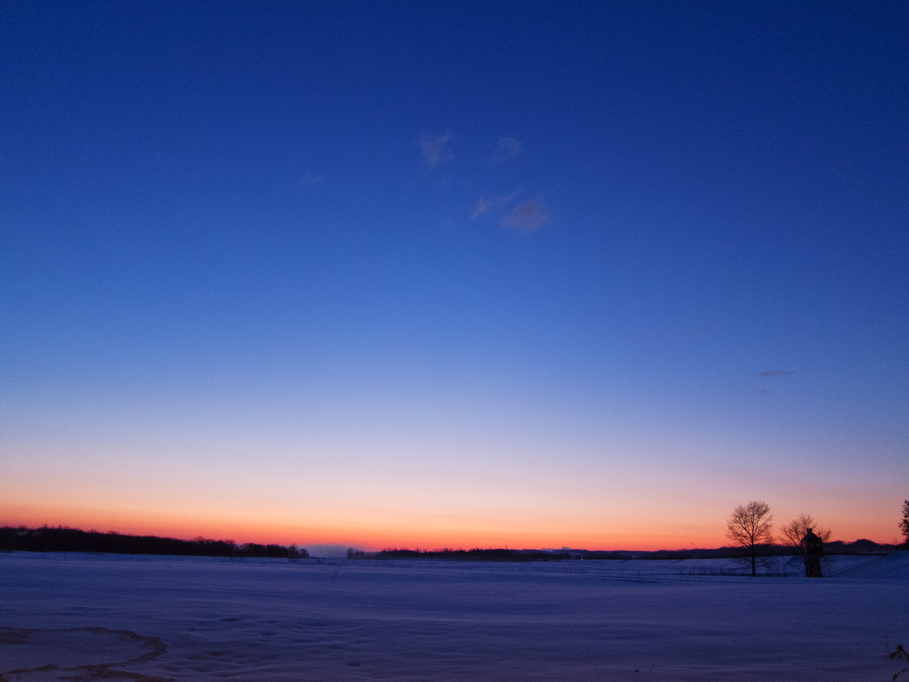 a snow covered field at dusk under the blue sky