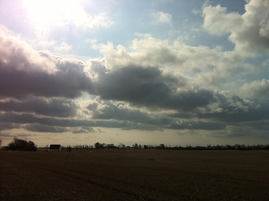 a large field with clouds and sun shining in the distance