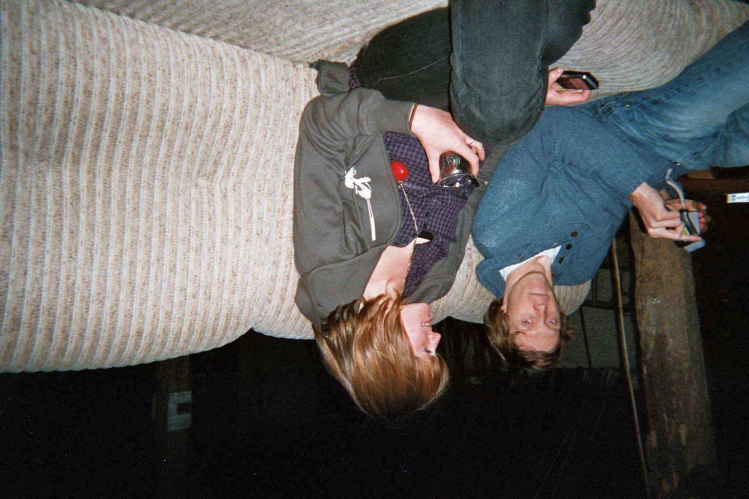 a person upside down on a bed, while a man drinks from a wine glass