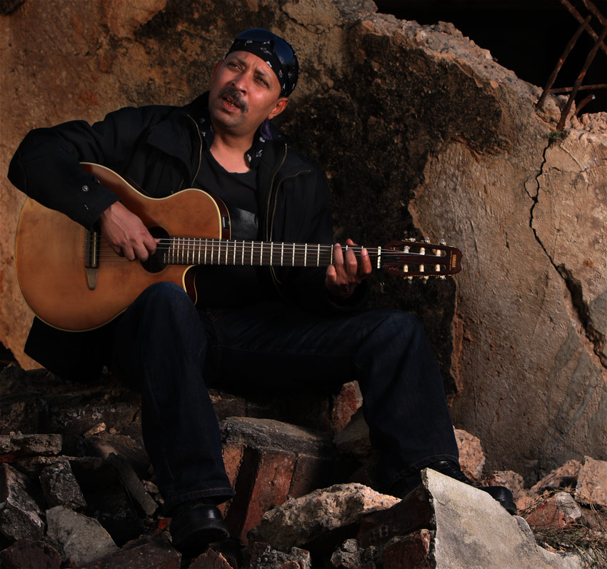 a man sitting in a pile of rocks holding an acoustic guitar