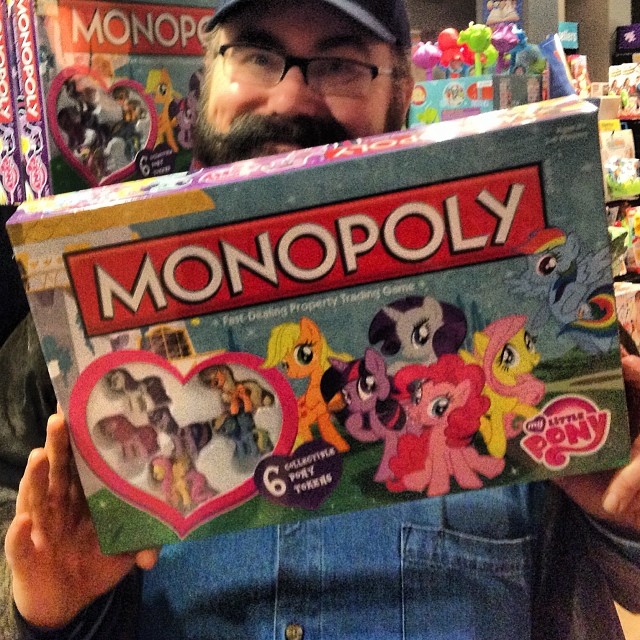 man in blue jeans holding up box of monopoly toys