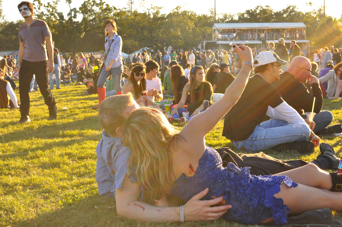 a group of people sitting in the grass and one man holding up his arms with his other hand