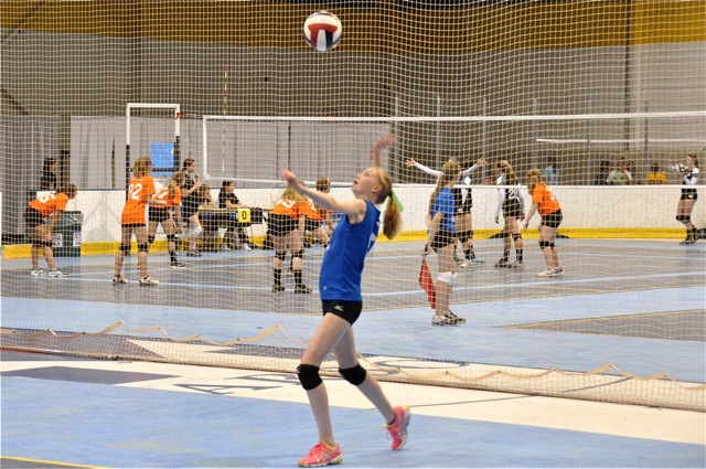 a lady jumping up to catch a ball while playing volleyball