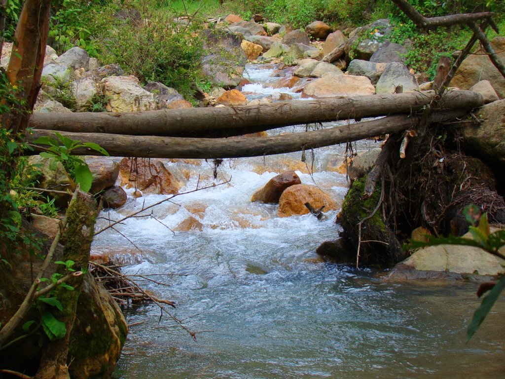 water flows under a wooden bridge, with rock walls