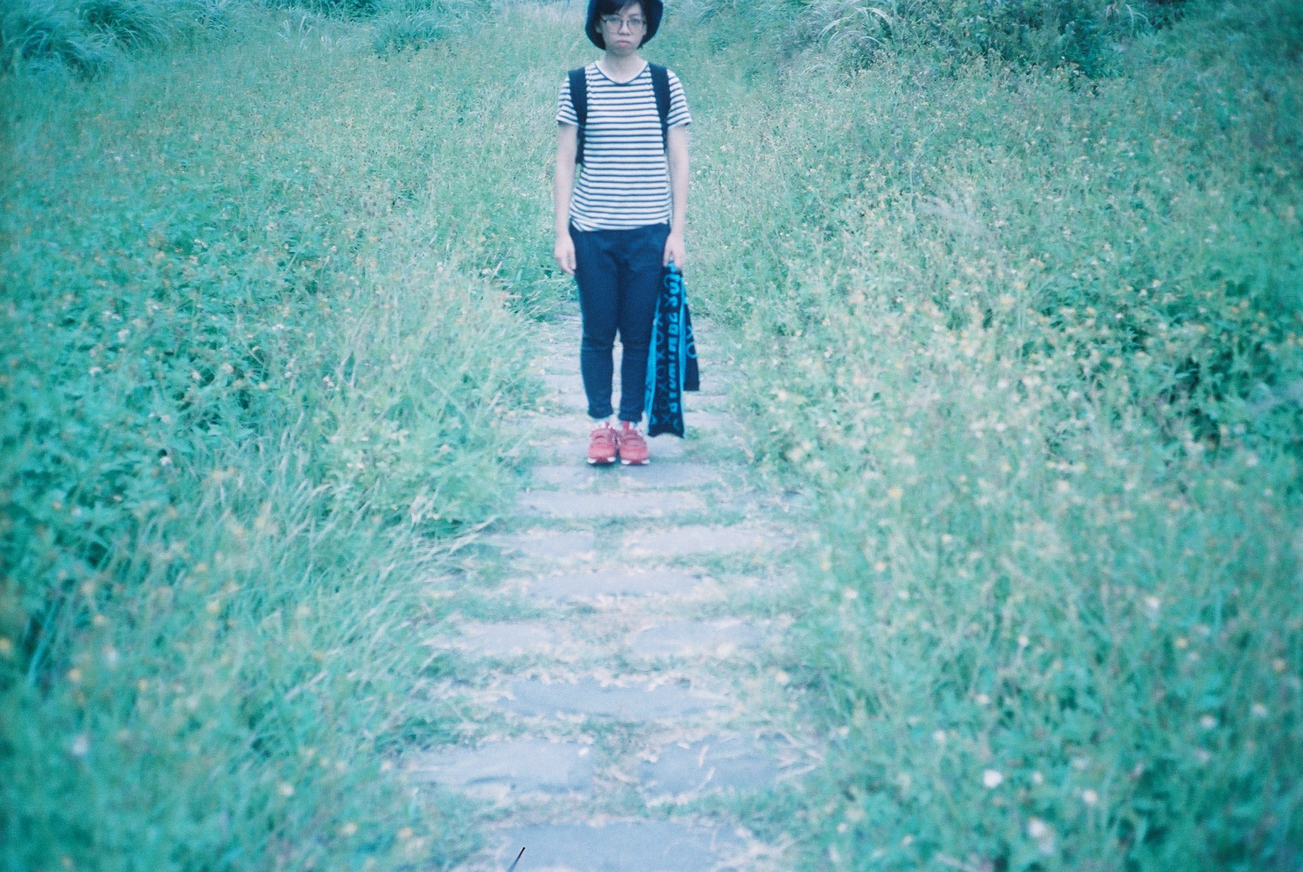 a woman stands on a path surrounded by tall grass