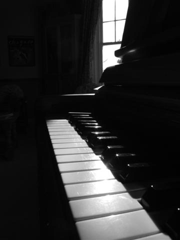 the shadow is cast on a piano, near the window