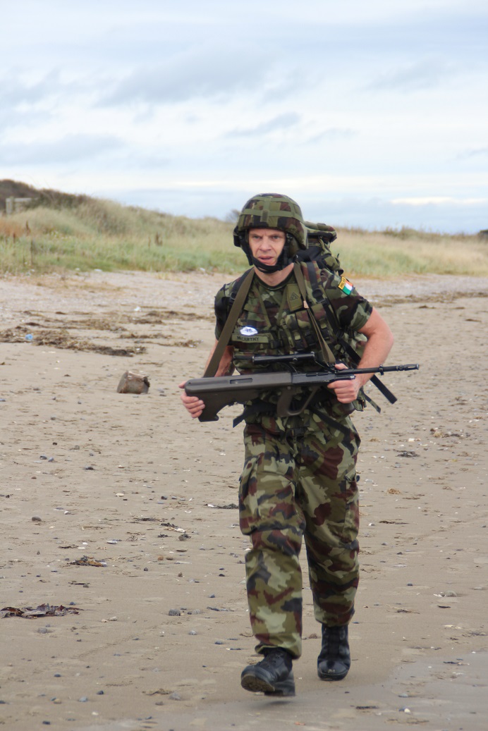 an armed man walking across a sandy beach
