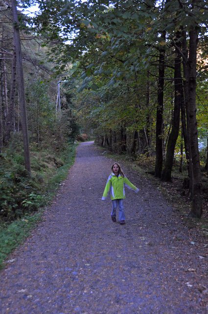 a little girl walking down a dirt road by trees