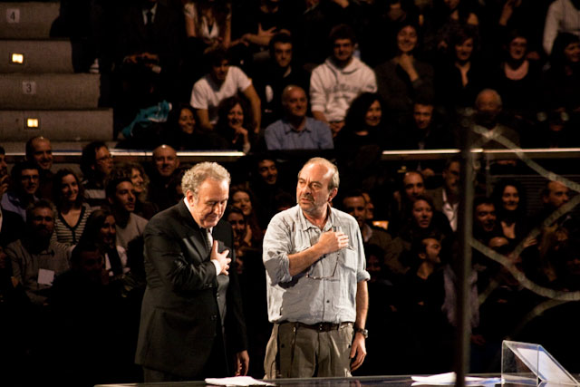 two men talking while they stand in front of an audience