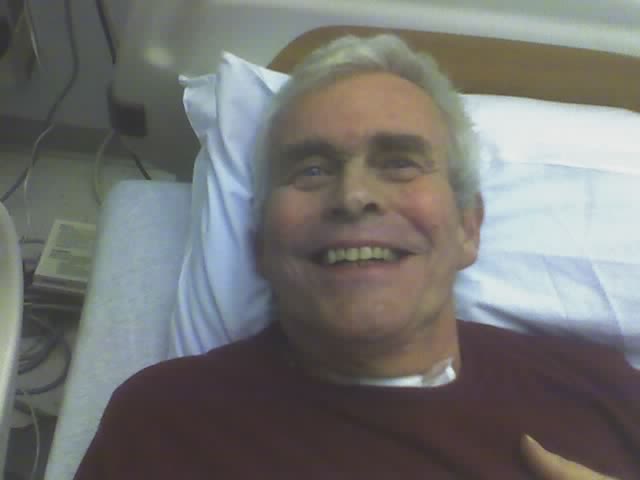 older man laying in bed smiling at the camera