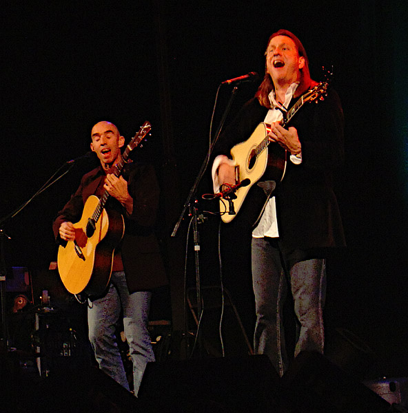 two people on stage playing guitar and singing