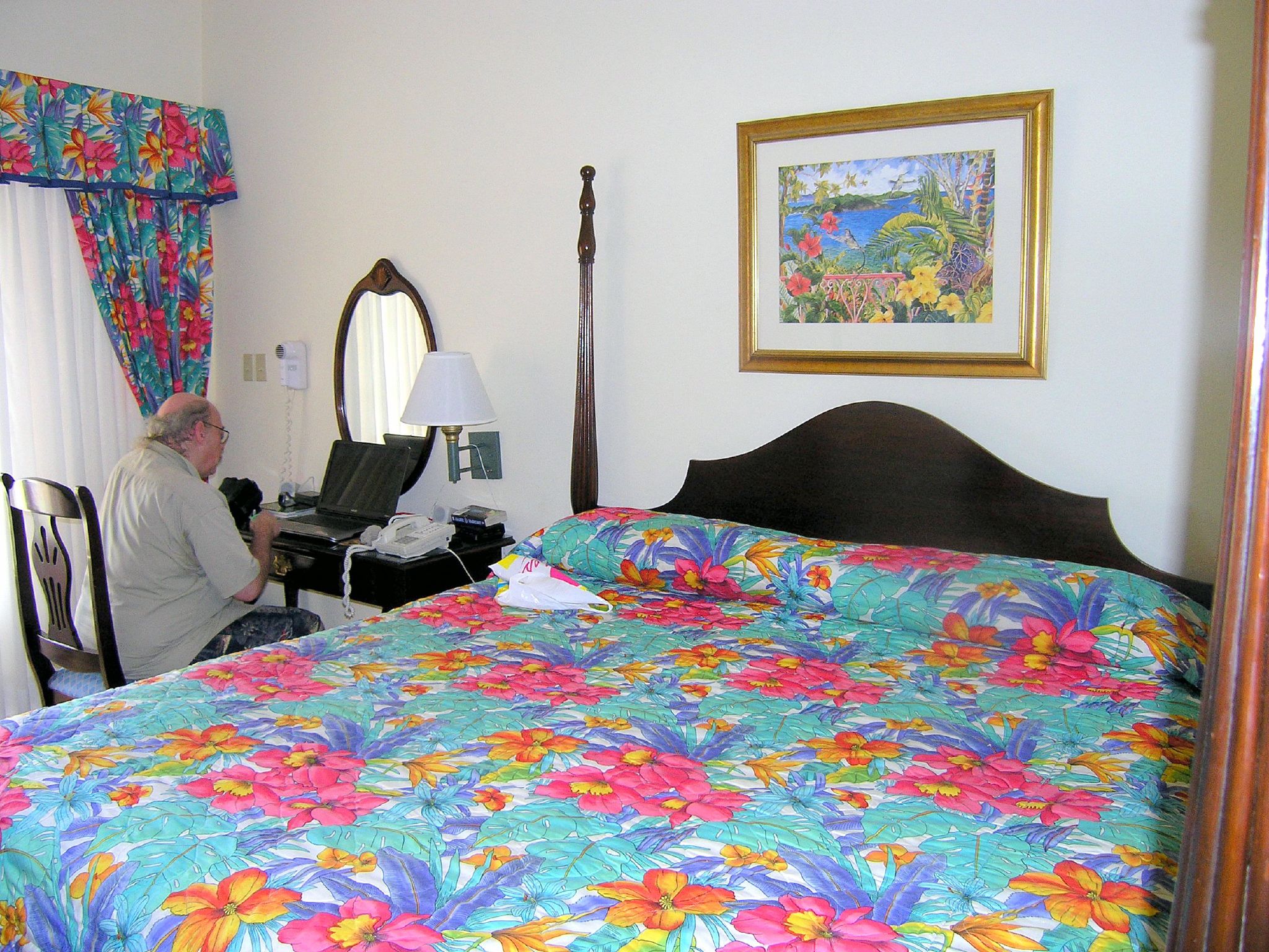 a man sitting in a el room with a large bed and mirror