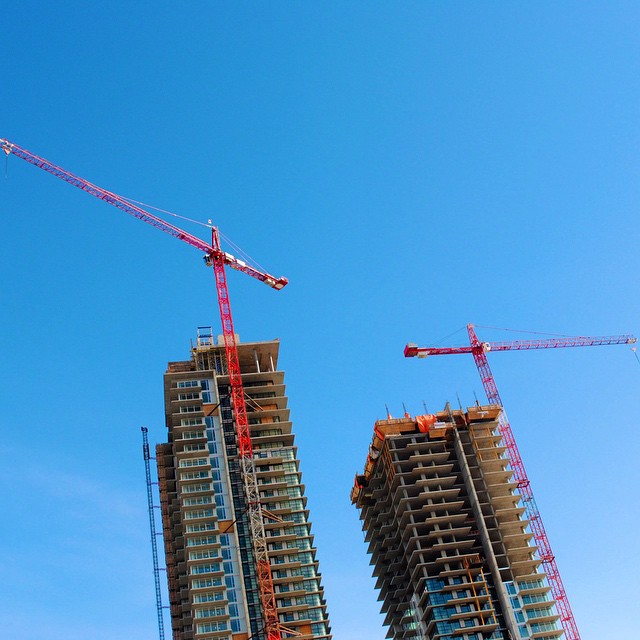 a group of cranes stand near large tall buildings