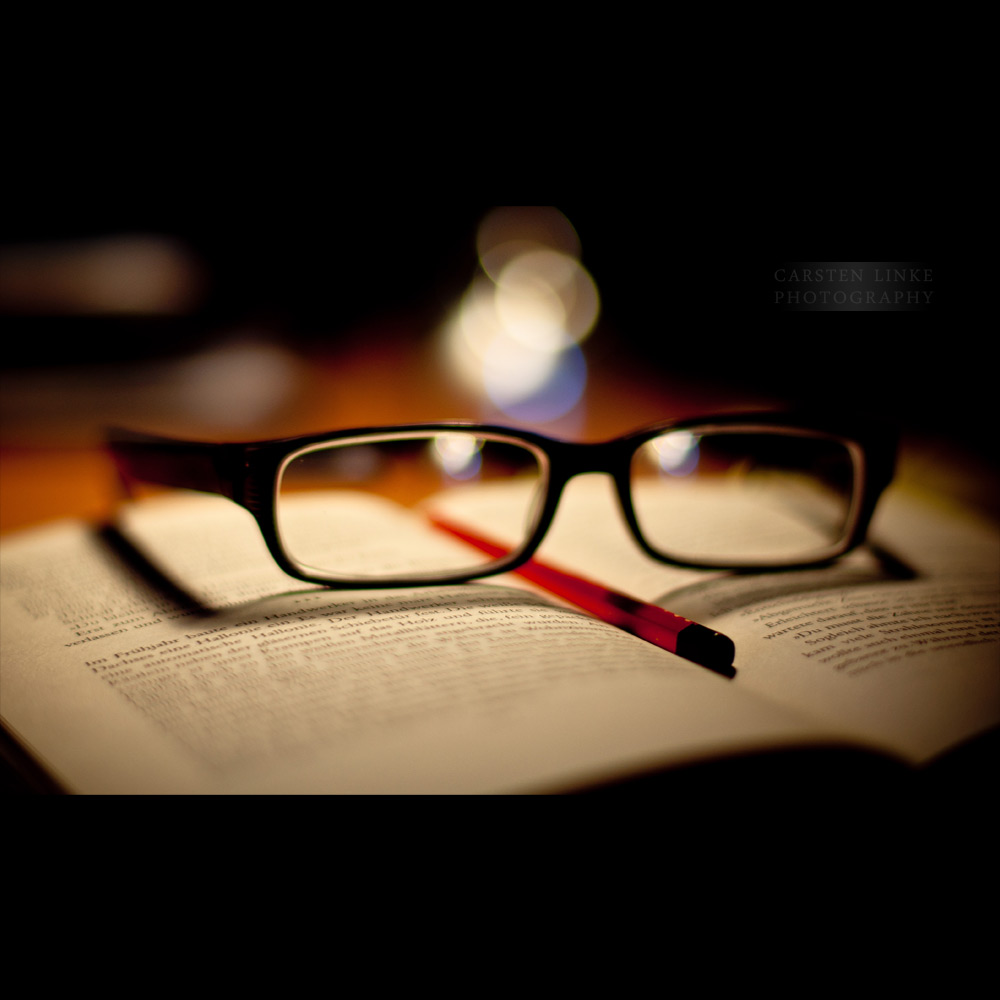 a book, glasses and pen are resting on a table