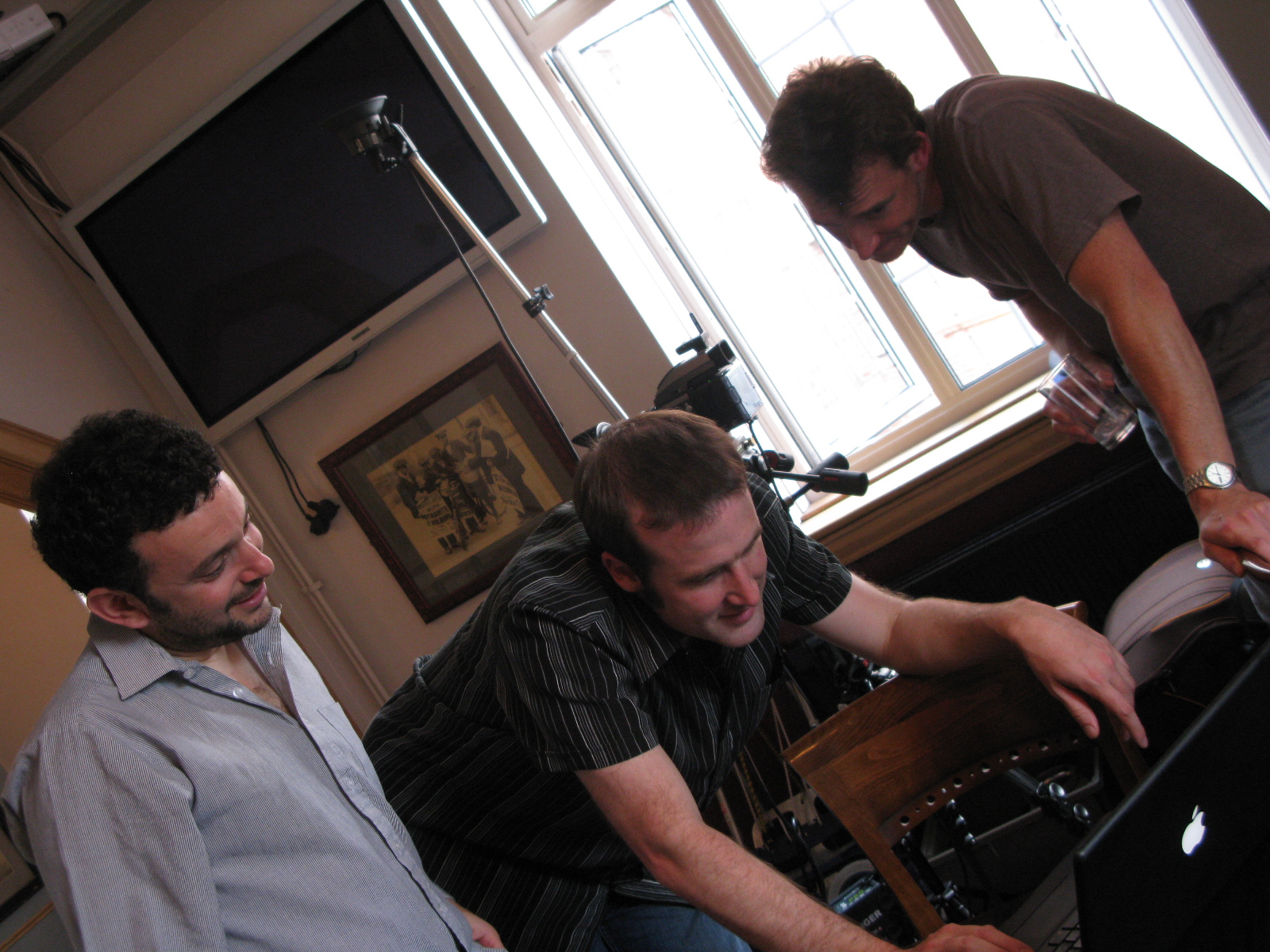 three men in a living room looking at soing on a keyboard