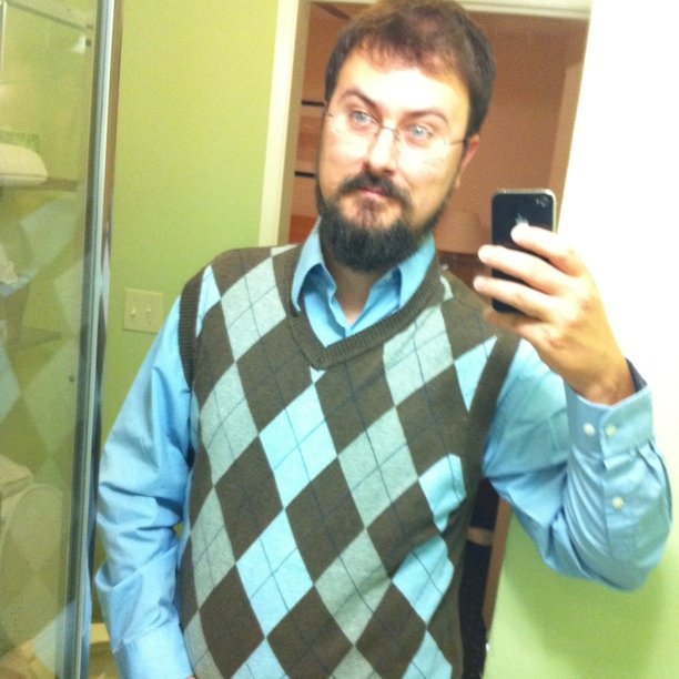 a man in glasses and sweater vest taking a picture of himself