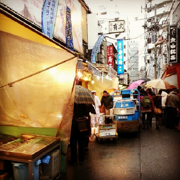 several people walking down an oriental market carrying umbrellas