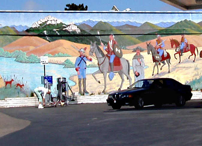 a car driving past a colorful mural near a gas station