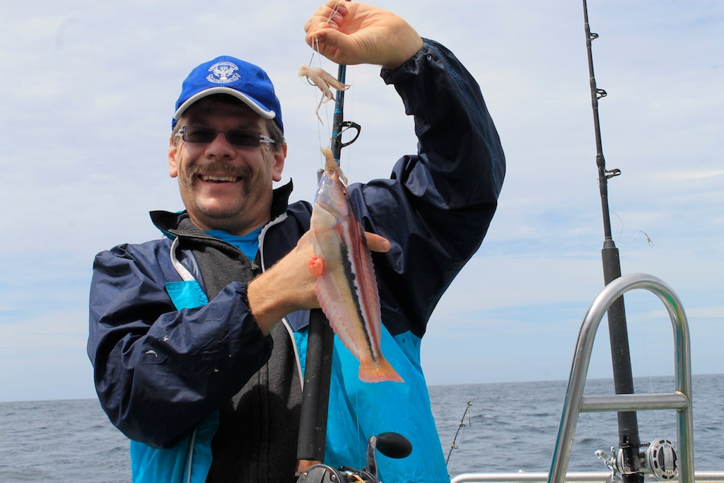 a man in blue jacket holding up fish in front of his head