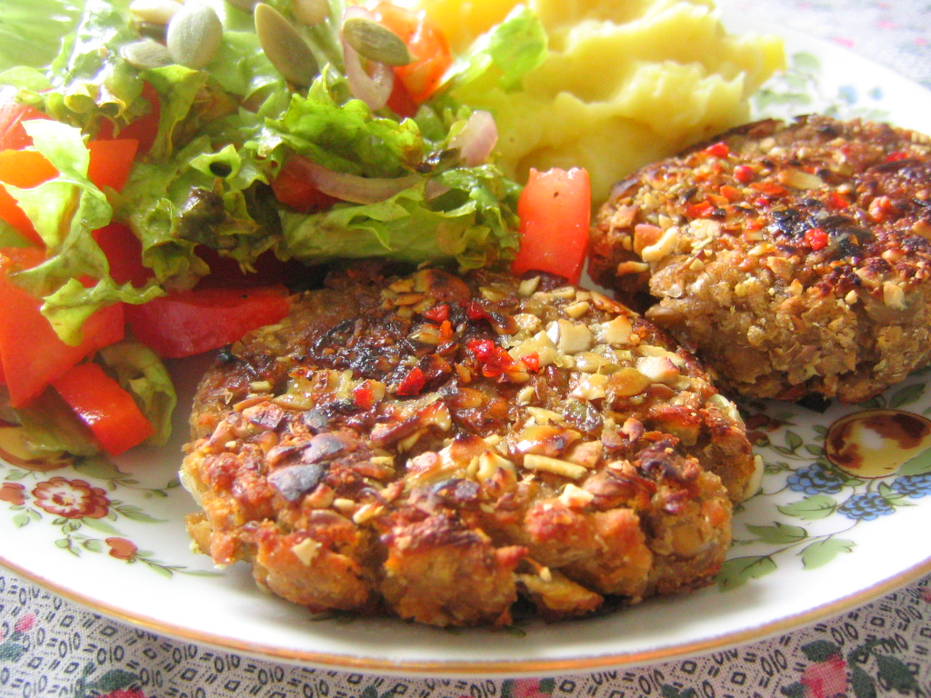 three burger patties sit on a plate with vegetables and potatoes