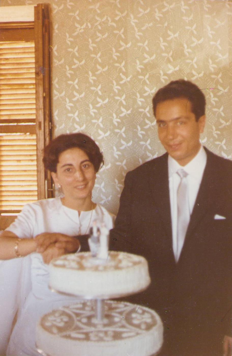 a woman in white dress and man in a suit standing by a table with a cake