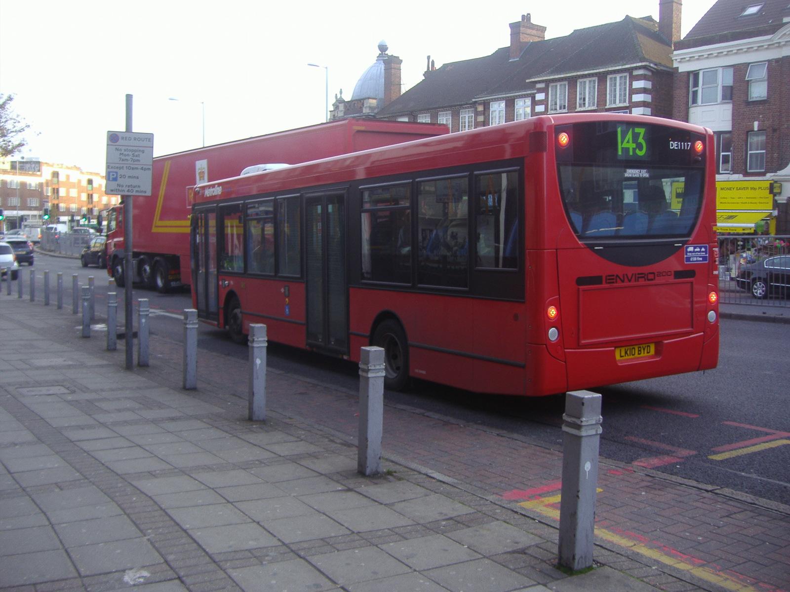 two red buses parked on side of road next to fence