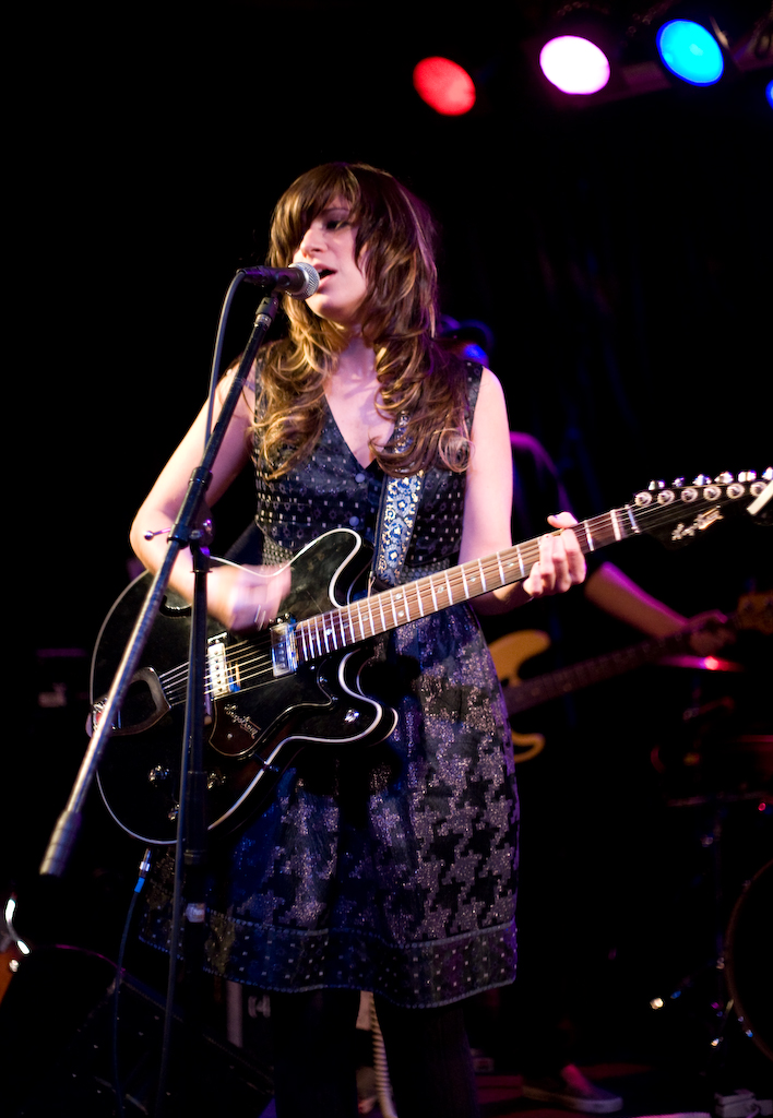 a woman holding a guitar and singing into a microphone