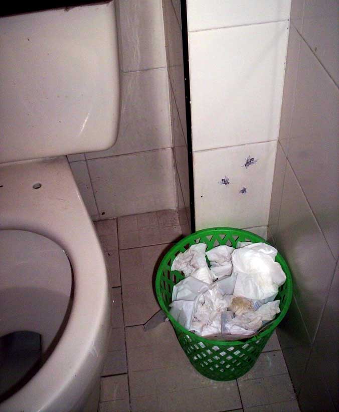 a bucket full of paper next to the toilet