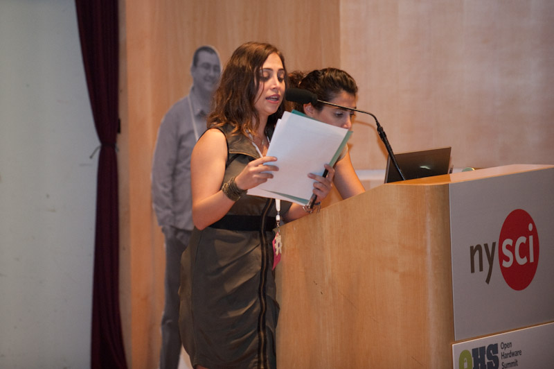 a woman in a dress reading from a folder in front of a microphone