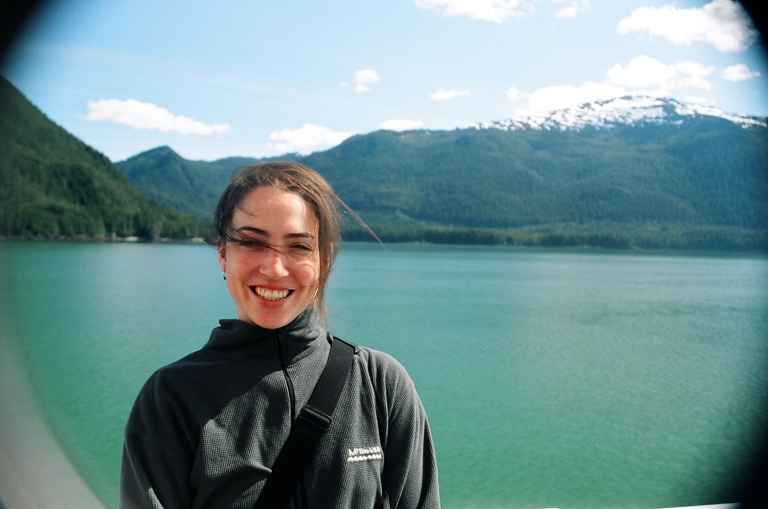 a young woman smiles near the water with a mountain in the background