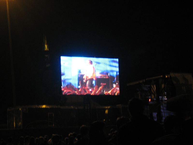 people watching the screen in a dark, outdoor area